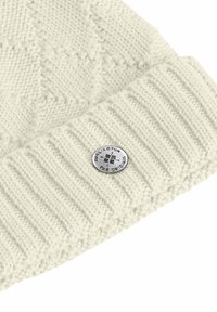 Cream-colored knitted beanie with a ribbed brim, featuring a silver logo button on the front and a textured, patterned body.