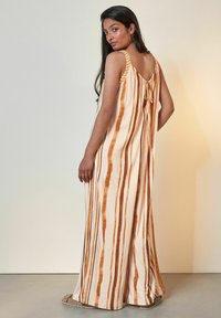 Rochie maxi cu detaliu de legare la spate, model rayat în nuanțe de bej și portocalie arsă, confecționată dintr-un material ușor, cu o croială lejeră.