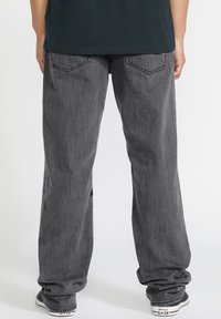 Pantalones de mezclilla gris con un corte relajado, que cuentan con bolsillos traseros y un ligero desgaste en la textura. Combinados con zapatillas negras.