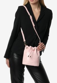 Borsa a secchiello in pelle sintetica di coccodrillo rosa con chiusura a coulisse e tracolla regolabile. Texture liscia, forma compatta e dettagli dorati.