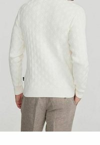 Biały sweter dziany z teksturowanym wzorem warkocza, okrągłym dekoltem i długimi rękawami, zestawiony z jasnoszarymi spodniami.