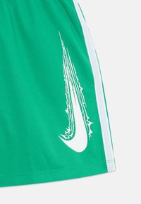 Pantalones cortos deportivos verdes hechos de una tela de malla ligera. Presentan una franja blanca a los lados y un logo estilizado en blanco impreso en la pierna izquierda.