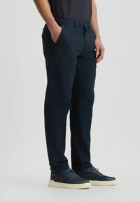 Marineblaue Hose mit geradem Bein, elastischem Bund, Seitentaschen und dezenten Faltenlinien. Kombiniert mit dunklen Sneakers.