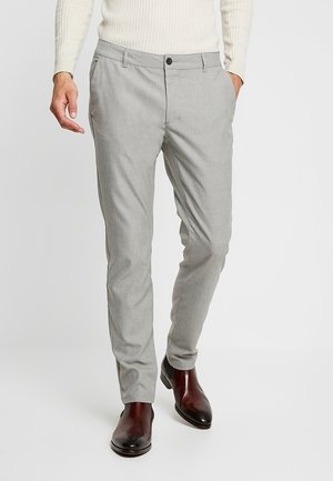 Mand iført lysegrå slim fit bukser, off-white ribbet sweater og mørkebrune læder festsko, der går fremad.