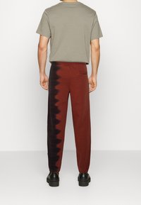 Rote und schwarze Batik-Hosen mit schmal zulaufendem Bein, elastischem Taillenbund und Gesäßtasche, kombiniert mit einem grauen T-Shirt mit kurzen Ärmeln.