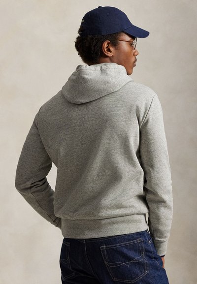 Γκρι βαμβακερό φούτερ με κουκούλα και κορδόνι, φορεμένο με σκουρόχρωμο μπλε τζιν. Το σχέδιο διαθέτει ριμπ μανσέτες και τελείωμα, με απαλή υφή.