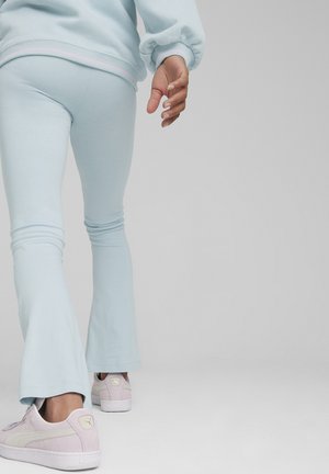 Leggings acampanados de color azul claro, hechos de una tela suave, combinados con zapatillas blancas y moradas claras que tienen un logo en el talón.