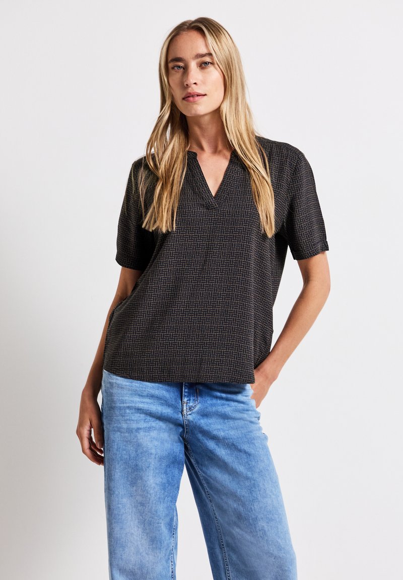 Kurzärmliges schwarzes Oberteil mit einem dezenten geometrischen Muster, V-Ausschnitt und lockerem Schnitt, kombiniert mit hellblauen Jeans.