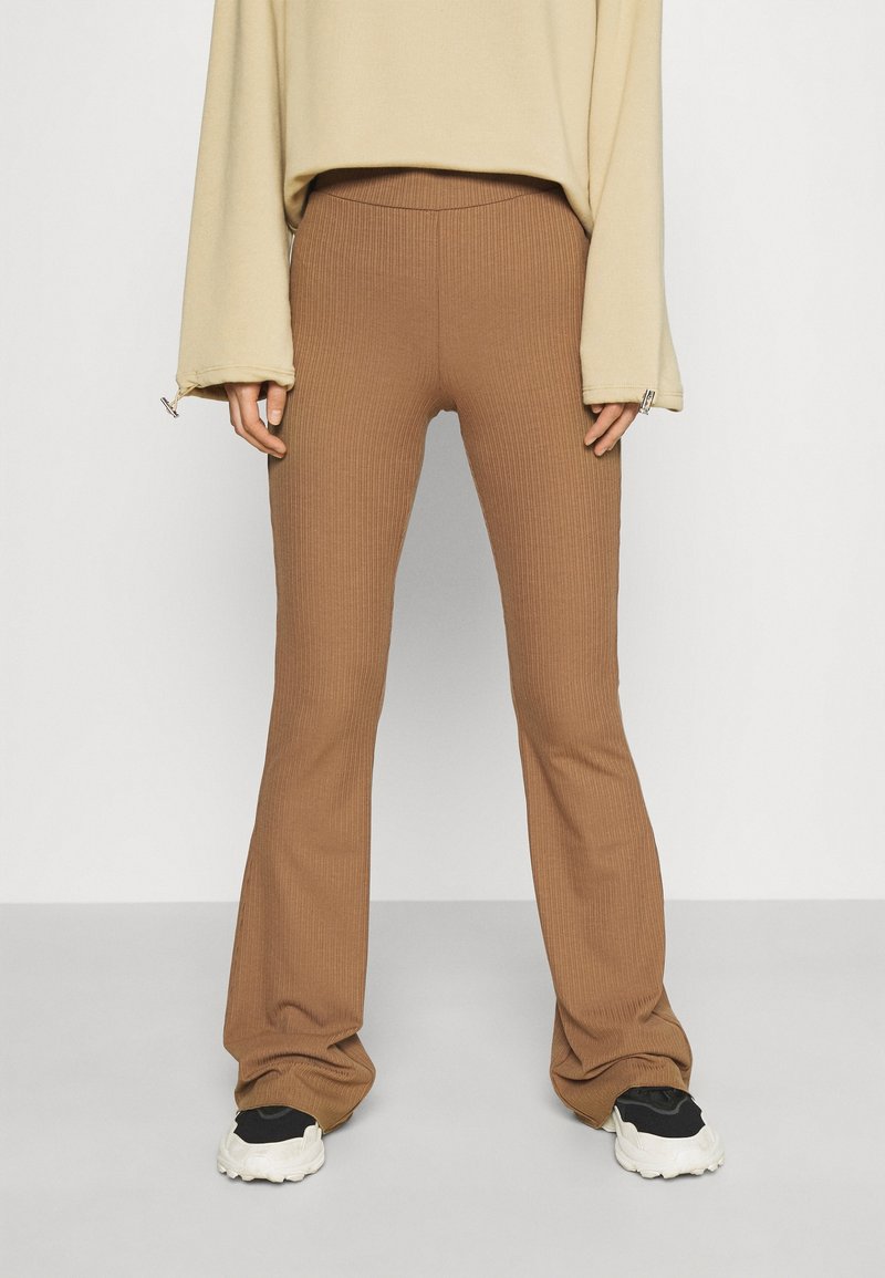 Pantalon évasé côtelé marron avec une taille confortable, associé à des baskets noires et blanches. Le tissu présente une finition texturée.
