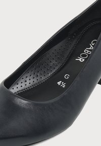 Escarpin femme en cuir noir avec semelle intérieure perforée, étiqueté taille 4,5 et largeur G, montrant une partie du nom de la marque Gabor à l'intérieur.