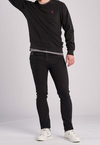 Felpa nera con logo rosso, abbinata a jeans skinny neri e sneakers bianche. I materiali sembrano morbidi e aderenti.