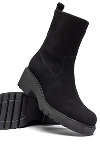 Stivaletti neri in suede con una suola in gomma spessa, punta arrotondata e una linguetta sul retro per una facile vestibilità. Dettagli di cucitura minimi visibili.