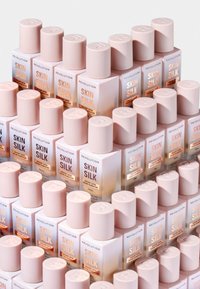 Stablede flasker med Revolution Skin Silk serum; uigennemsigtig glas med en gradient fra hvid til fersken, beige kapsler, minimalistiske etiketter med logo.