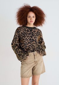 Suéter de estampado de leopardo en marrón y negro, con un cuello negro de canalé y mangas oversized, combinado con pantalones cortos de mezclilla beige.