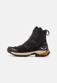 Bota de senderismo negra con diseño de caña alta, parte superior sintética, cuello acolchado y suela de goma robusta con tacos de tracción. Logotipo de "Salewa" visible.