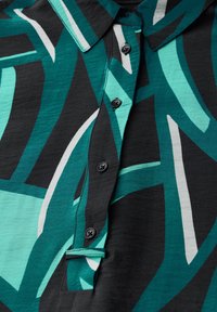 Camicia a maniche corte con bottoni, caratterizzata da una base in tessuto nero con grandi motivi astratti in teal e bianco, comprendente un colletto alla francese e bottoni neri.