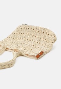 Geweven stro tote tas in beige met een gestructureerd patroon, voorzien van twee stevige handvatten en een bruine leren accenten met metalen drukkers.