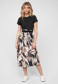 Haut noir à manches courtes associé à une jupe mi-longue ornée d'un motif de feuilles beige, noir et blanc. Accentué d'une taille noire.