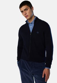 Cardigan blu navy con zip, realizzato in tessuto strutturato, con collo alto, polsini a coste e un piccolo dettaglio logo sul petto.