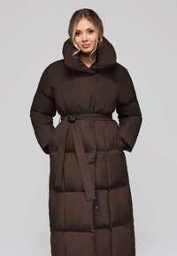 Piumino marrone con collo alto, cintura in vita e texture trapuntata. Presenta maniche lunghe e un design di lunghezza media.