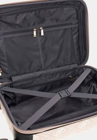 Valise rigide de couleur beige clair avec un motif matelassé. L'intérieur possède une doublure noire, une poche zippée en maille et des sangles croisées pour sécuriser les objets.