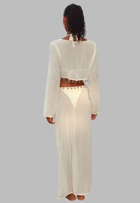 Tenue en tissu blanc transparent comprenant un crop-top à manches longues, avec un lien à l'arrière, et une jupe longue ornée d'accents décoratifs.