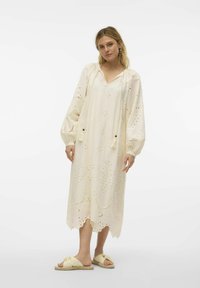Krämfärgad knälång klänning med broderi, dragsko i halsen och puffärmar. Tillsammans med ljusgula slip-on sandaler.