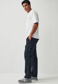 Weißes kurzärmliges T-Shirt, marineblaue Cargo-Hosen mit mehreren Taschen und graue Sportschuhe mit weißen Akzenten. Einfaches, funktionales Design.