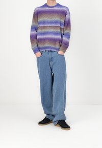 Pull rayé aux teintes violettes, bleues et grises ; jean denim bleu clair à coupe décontractée et taille haute ; baskets noires à semelle en gomme.