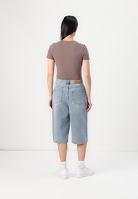 Top marrón de manga corta y pantalones cortos de mezclilla azul claro con un ajuste relajado, con bolsillos traseros y una etiqueta de marca de cuero beige en la cintura.