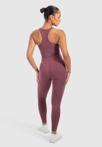 Maroon sportieve bodysuit met een racerback ontwerp en een getailleerde pasvorm, gecombineerd met witte sneakers. Soepele textuur, logo zichtbaar op de taille.