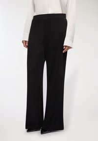 Czarne szerokie spodnie o fakturowanym wykończeniu, z wysokim stanem i płynącą sylwetką, połączone z białą bluzką z długim rękawem.