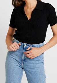 Svart randig pikétröja med v-ringning och korta ärmar, kombinerad med högmidjade ljusblå jeans.