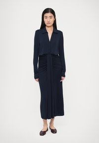 Navy long-sleeve dress with a buttoned v-neck, gathered waist, and a straight skirt. Soft fabric with a smooth texture. Flat brown shoes.