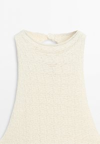Close-up of cream-colored knitted sleeveless top with round neckline and button closure at the back.