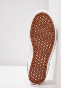 Kenkänsäntä, jossa on teksturoitu kumipinta, jossa on timanttimainen kuvio. Se on reunustettu valkoisella välikannalla ja harmaalla ja vaaleanpunaisella sivuyksityiskohdalla.