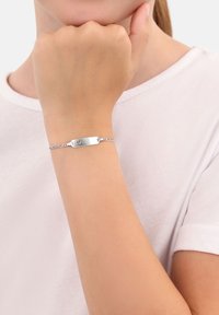 Niño con una pulsera de cadena de plata con un corte en forma de corazón en la placa sobre una camiseta blanca.