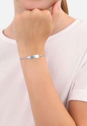 Niño con una pulsera de cadena de plata con un corte en forma de corazón en la placa sobre una camiseta blanca.