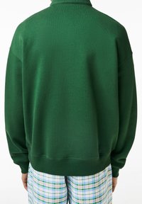 Sweat-shirt vert oversize avec col montant et poignets côtelés. Le dos a une texture lisse, associé à un short en tartan à motifs.