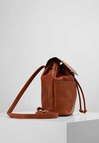Borsa a secchiello in pelle marrone con superficie testurizzata, dotata di chiusura a coulisse e tasca laterale, completata da una lunga tracolla.