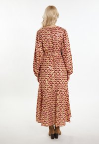 Rochie maxi cu mâneci lungi, cu un model de scoică roșie și aurie, talie strânsă și fustă fluidă; asortată cu botine maronii cu toc.
