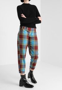 Pull noir à manches longues, pantalon à carreaux bleu, rouge et jaune, ourlet retroussé, associé à des bottines noires brillantes avec fermeture éclair.