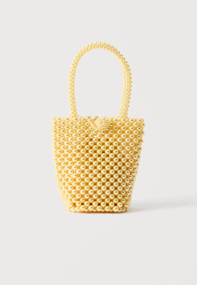 Petit sac à main style bocal fait de perles crème brillantes avec une anse en perles bouclée et une fermeture décorative avec un nœud de perles.