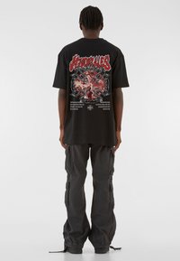 Must musta särk, mille taga on punase ja halli disainiga graafika, kantud tumedate cargo-pükste ja mustade jalatsitega.