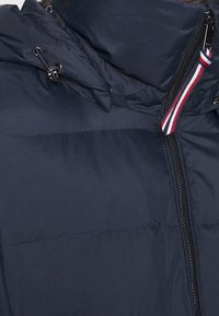 Marineblå dunjakke med høj krave, frontlynlås og stribede detaljer. Materialet ser glat og isoleret ud.