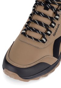 Beżowe syntetyczne buty trekkingowe z czarnym gumowym czubkiem, teksturowaną powierzchnią, czarno-białymi sznurówkami w wzór oraz subtelnymi detalami przeszycia.