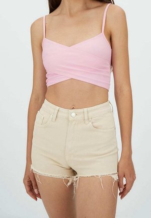 Femme portant un top court rose clair à fines bretelles et un short en denim beige taille haute avec des bords effilochés.