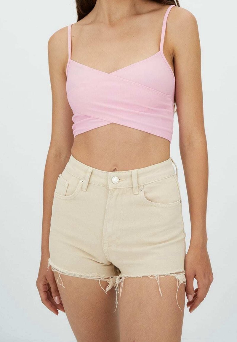 Femme portant un top court rose clair à fines bretelles et un short en denim beige taille haute avec des bords effilochés.