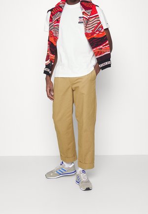 Camisa blanca bajo un sudadera de patrones multicolores, pantalones cortos beiges, y zapatillas grises con rayas azules. Conjunto casual y vibrante.