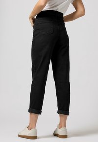 Jeans in denim nero con una vestibilità rilassata, risvolti, tasche posteriori e vita alta. Abbinati a sneakers bianche. Texture liscia.